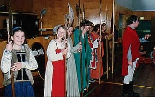 A group of students in medieval clothing. all holding pole weapons
